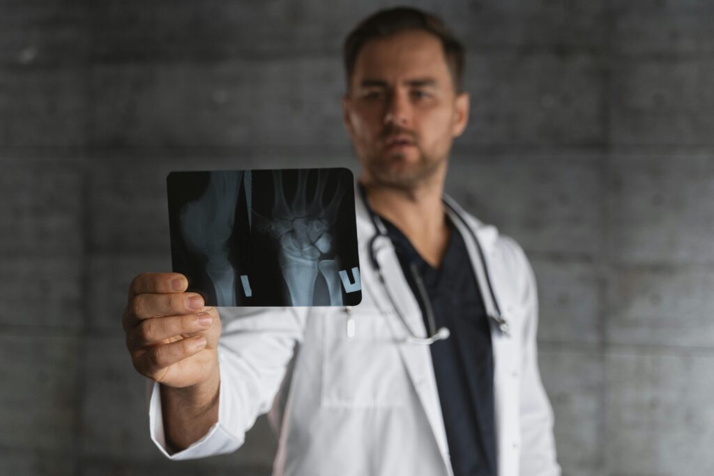Especialidades Disponibles A male doctor in a lab coat holding and examining an X-ray image in a clinical setting.